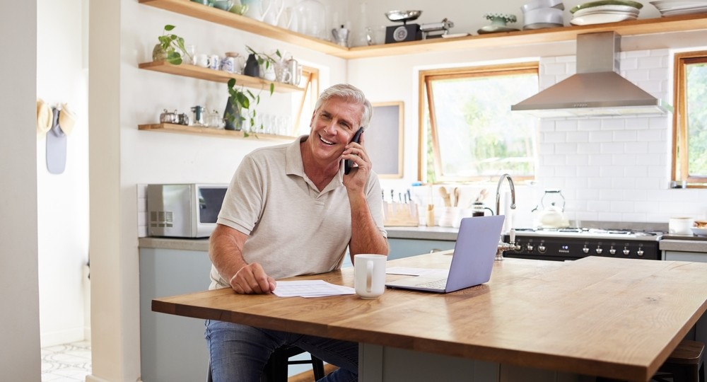 Happy senior man talking on his phone while using a laptop