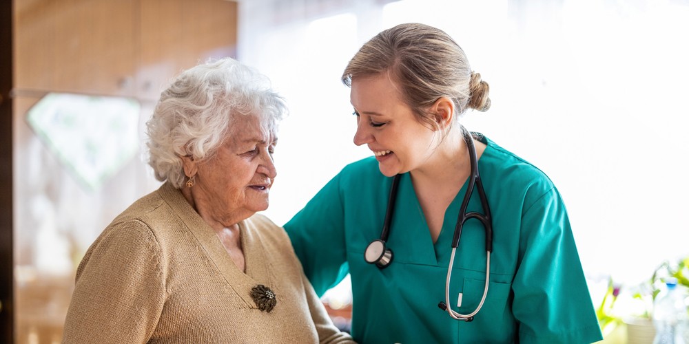 Female home carer supporting senior woman to stand up