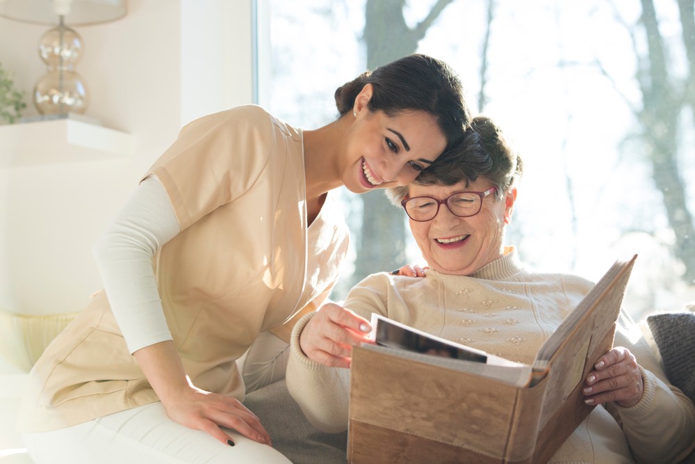 Happy senior woman smiling while looking a a photo album with her caregiver