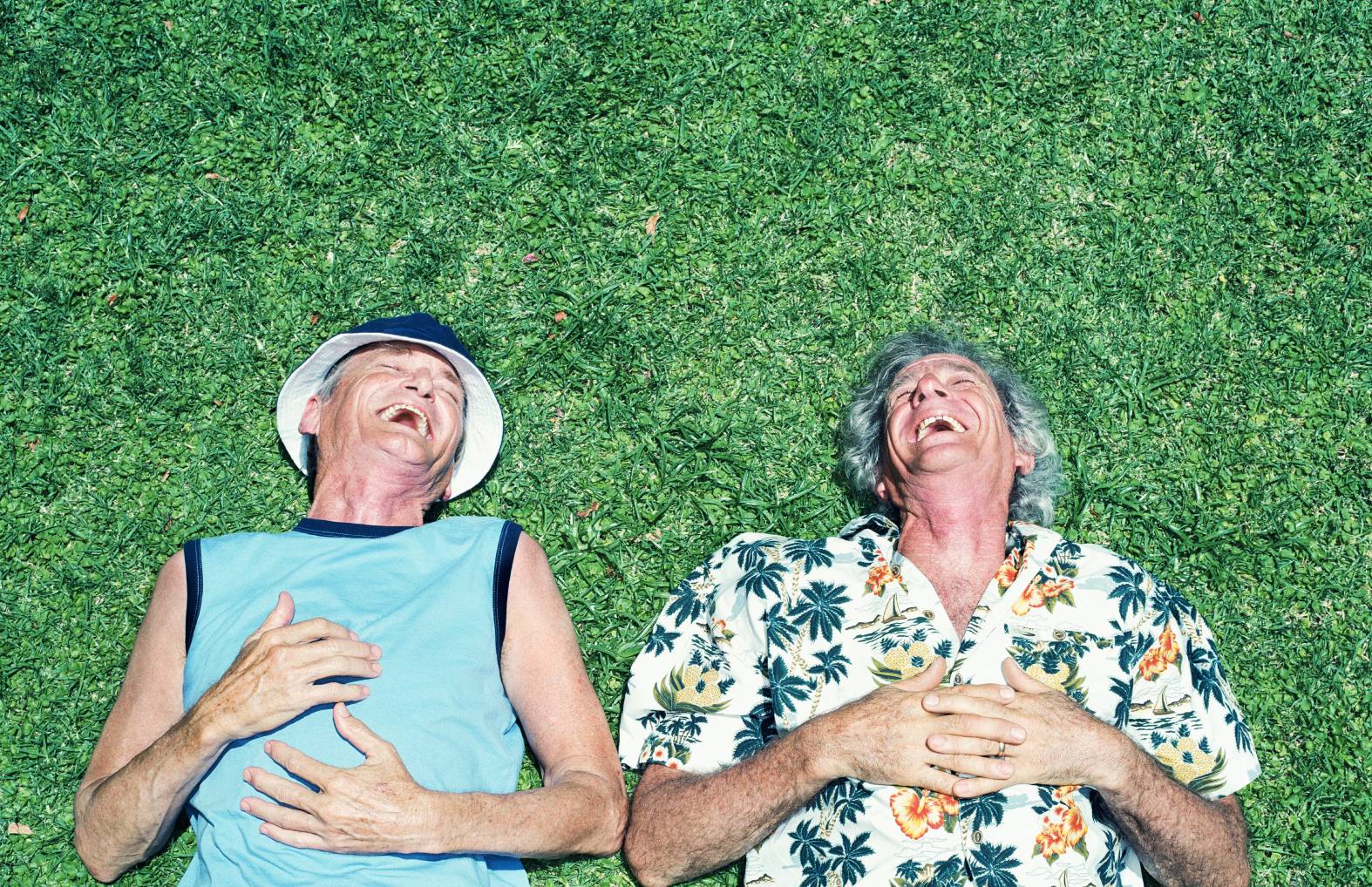 two older men laughing and laying down on grass outside