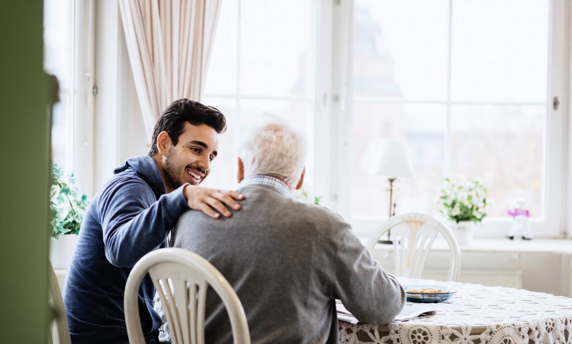 elderly man sitting down and talking with his adult son in a skilled nursing facility