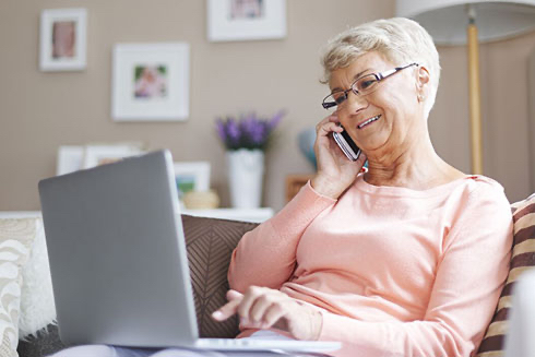 A senior woman talking on a cell phone and using a laptop.