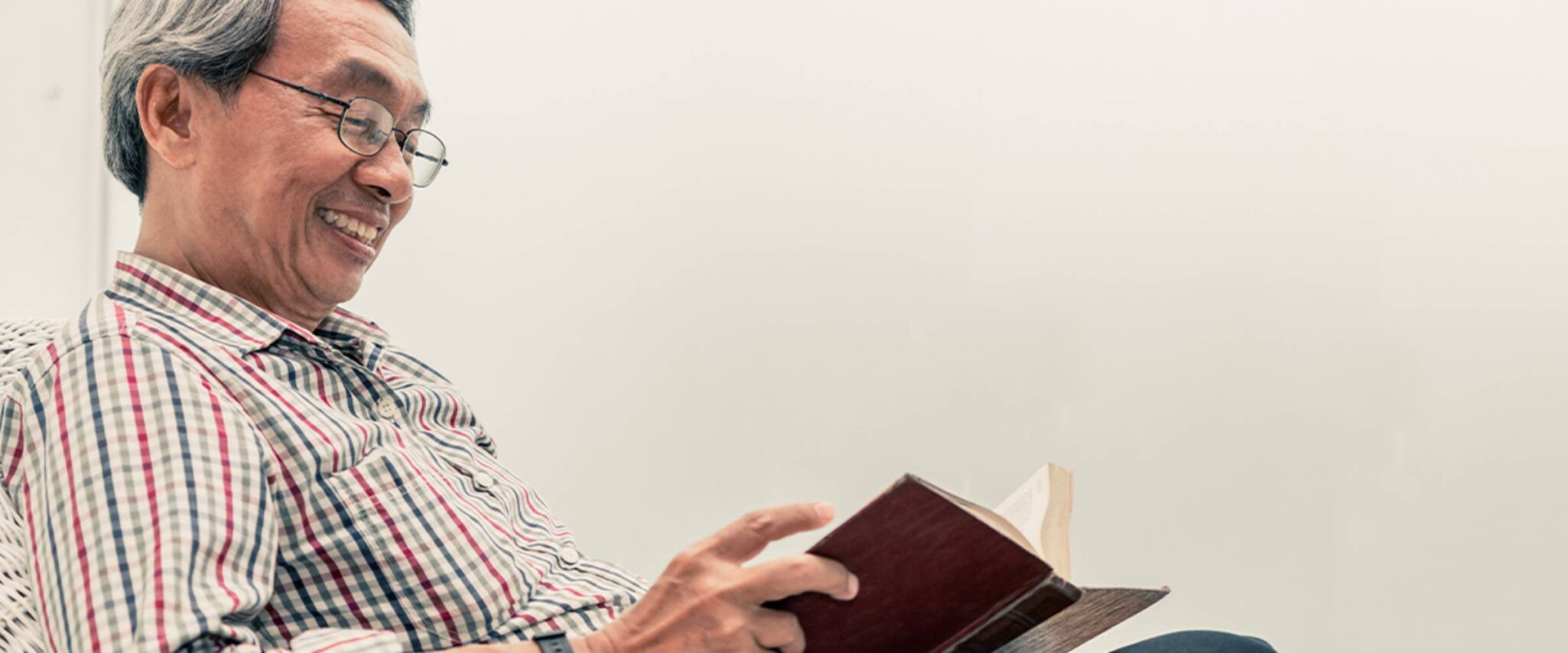 A senior man smiles while reading a book